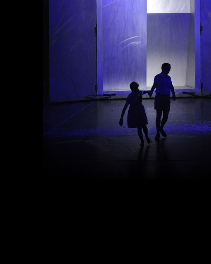 Two silhouettes walking hand in hand through a blue-lit doorway.