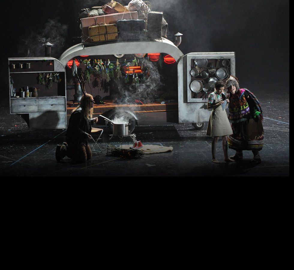 A caravan kitchen with a steaming pot over a fire, two figures beside it.