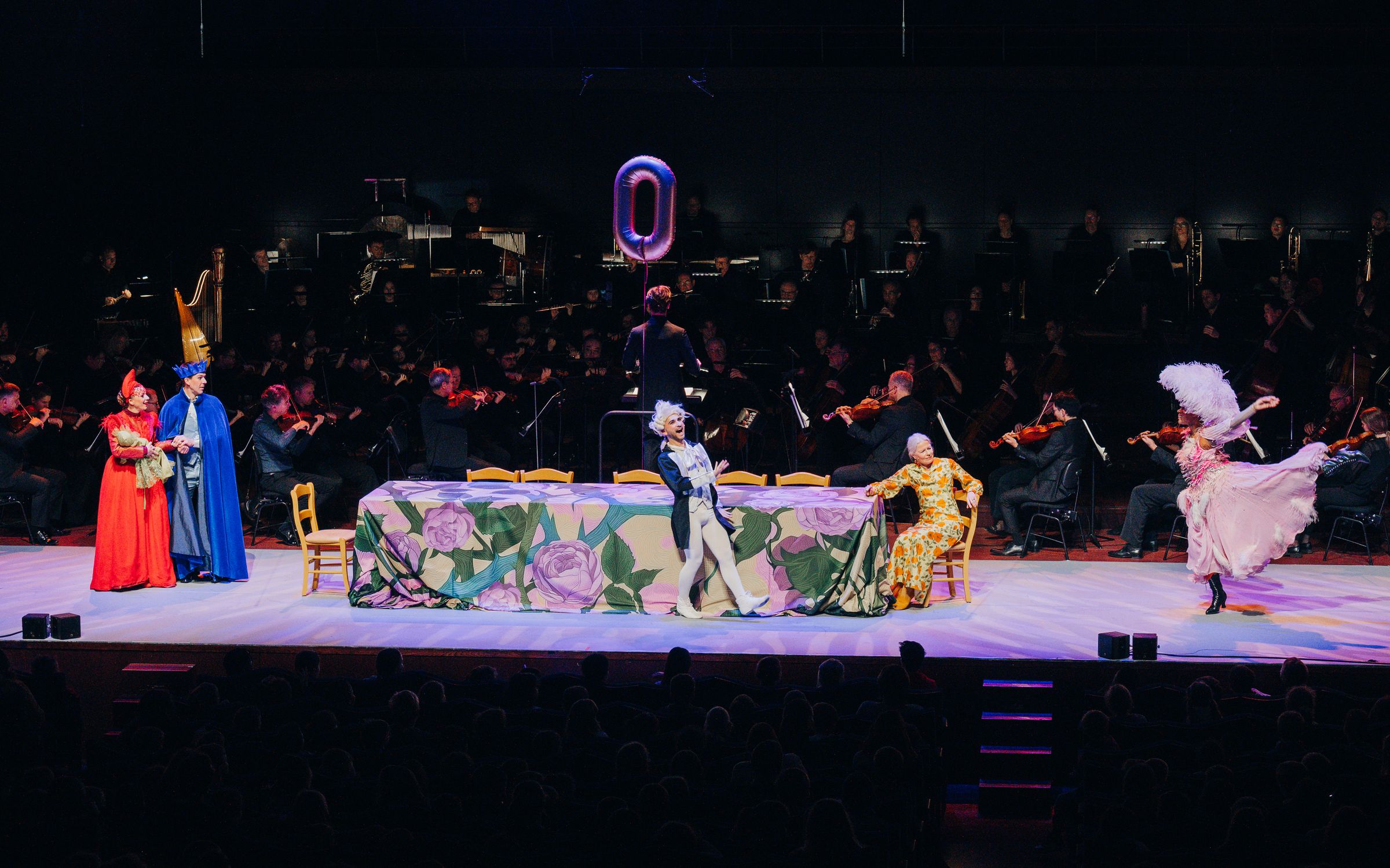 The stage in front of the orchestra: a long banquet table, the royal court and a dancer in white.