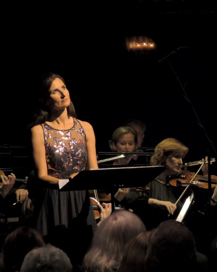 A singer in a sequinned dress in front of the orchestra.