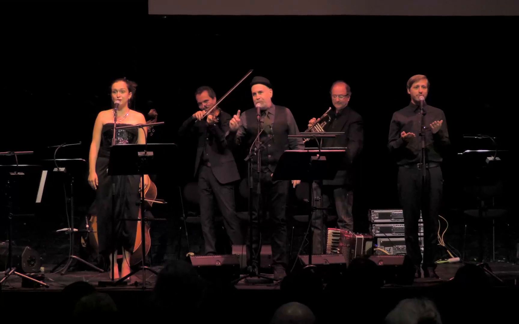 A singer and four musicians standing side by side on the dark stage.