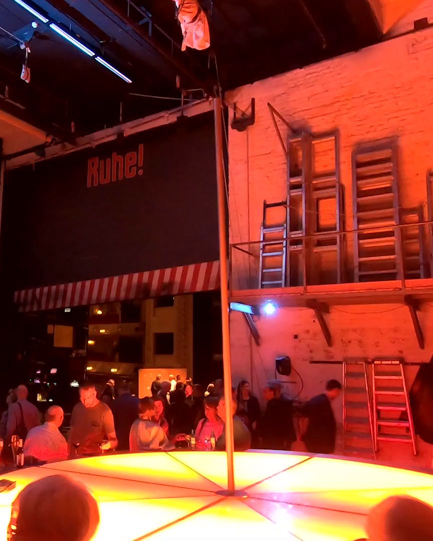 Red light, ladders on a brick wall and the audience around a glowing round platform.