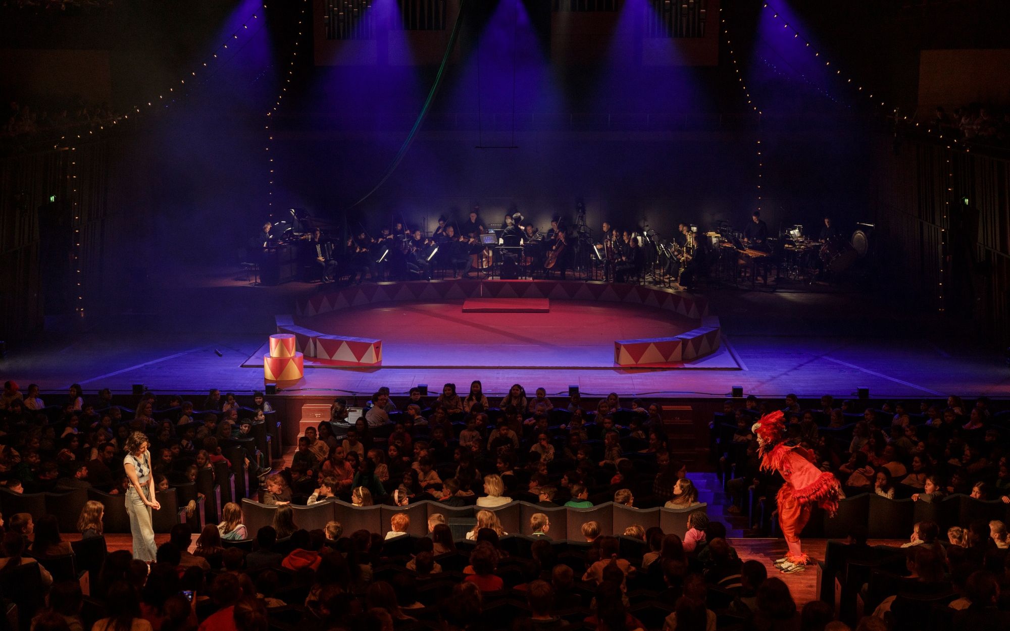 Wide view of the hall: the orchestra behind the red ring, the audience in front.
